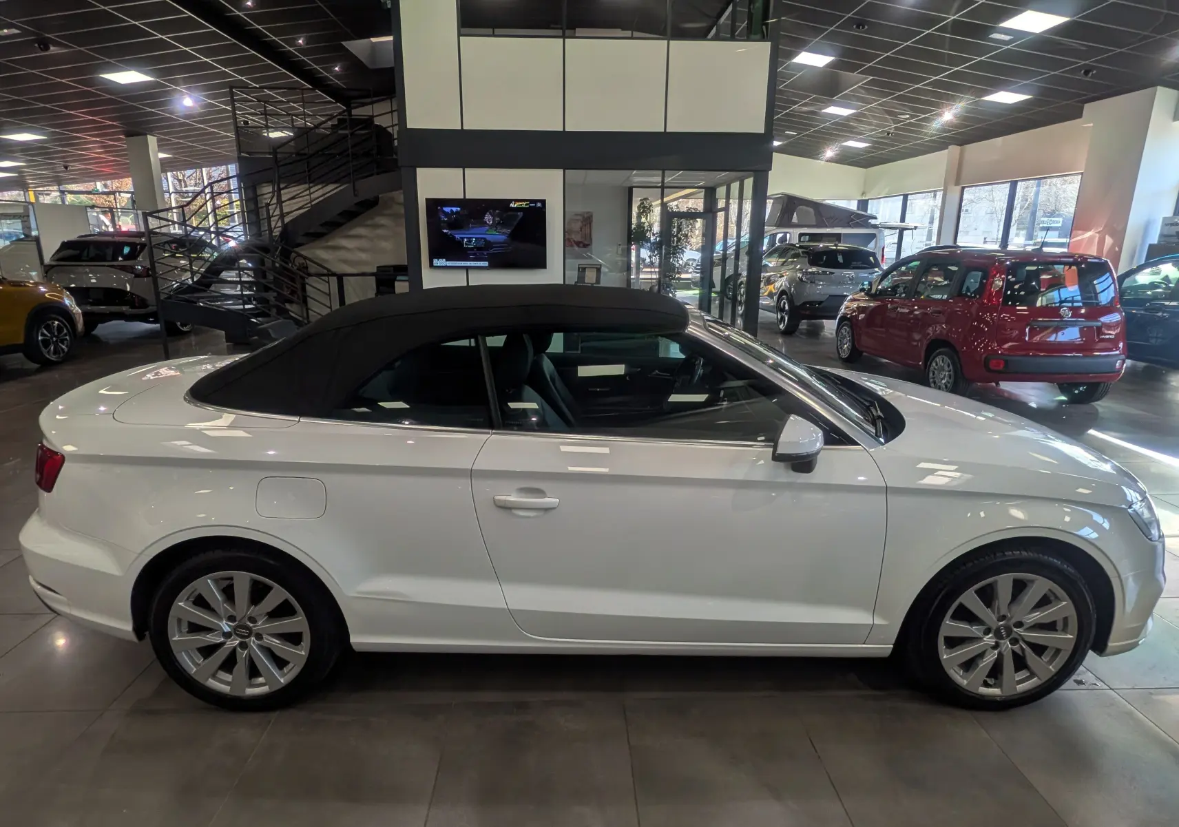 Audi A3 Cabriolet blanc vue de profil côté gauche avec toit noir fermé en intérieur showroom.