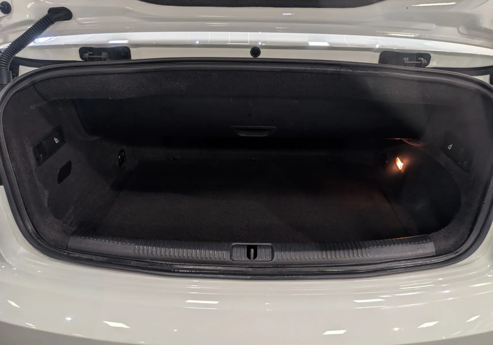 Coffre ouvert vu de face d’une Audi A3 Cabriolet blanche, intérieur noir avec éclairage latéral droit.