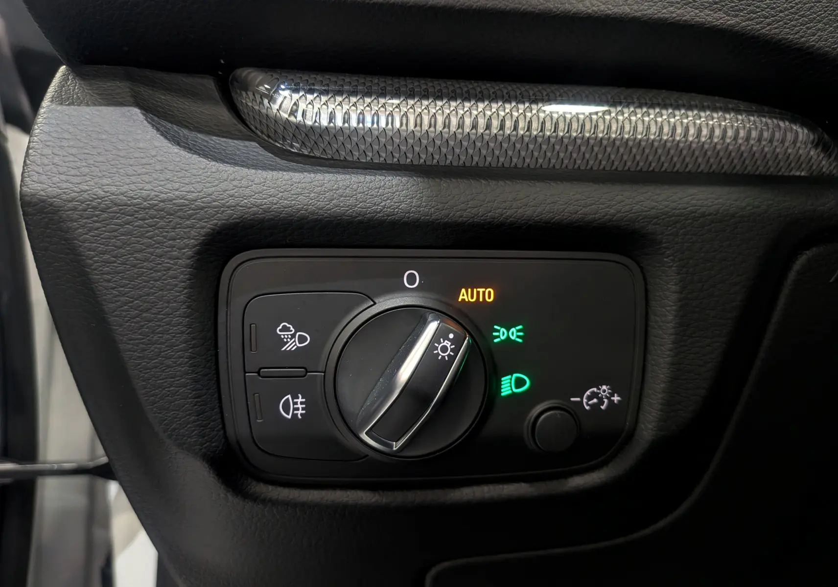 Gros plan sur le bouton de commande des phares avec réglage automatique, sur le tableau de bord noir de l'Audi A3 Cabriolet blanc.