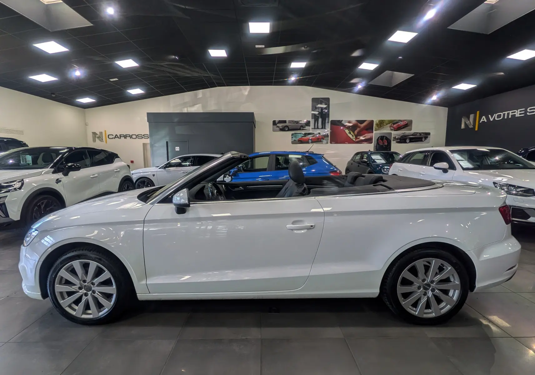 Audi A3 Cabriolet blanc vue de profil côté gauche, capote ouverte, intérieur noir visible en showroom.