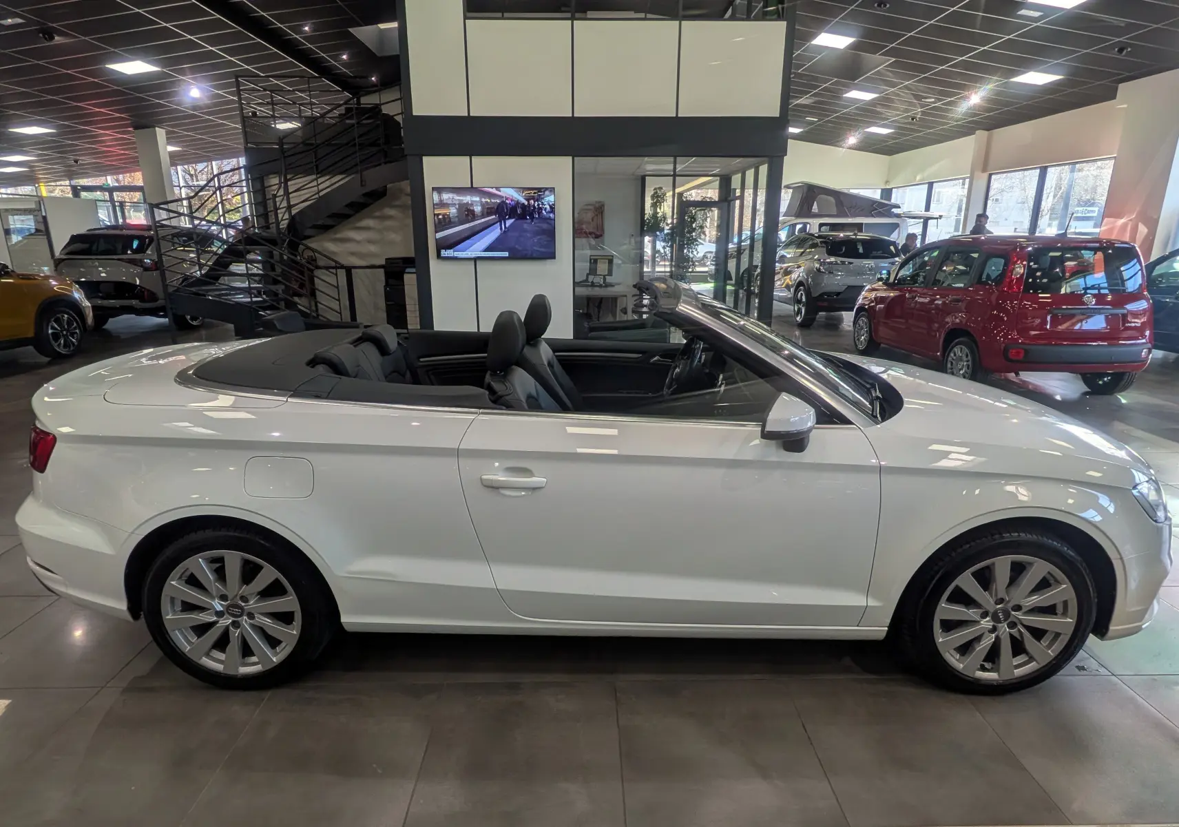 Audi A3 Cabriolet blanc vue de profil côté gauche, capote ouverte, intérieur noir visible en showroom.