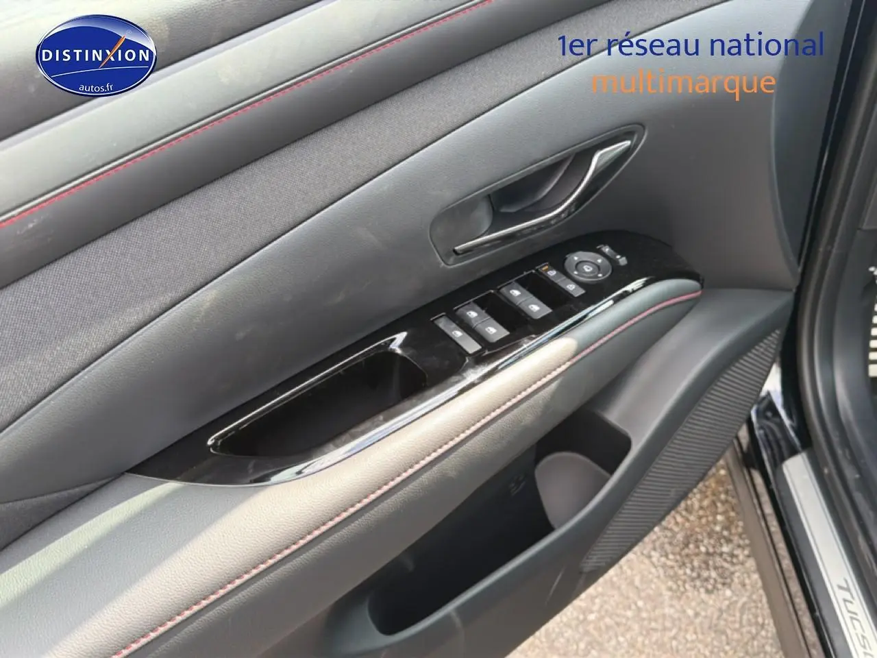 Gros plan sur la porte avant gauche noire du Hyundai Tucson 2026, avec commandes électriques et surpiqûres rouges.