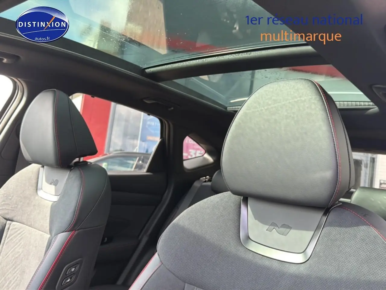 Vue intérieure du Hyundai Tucson noir 2026, sièges avant en cuir et alcantara avec surpiqûres rouges et toit panoramique en verre.