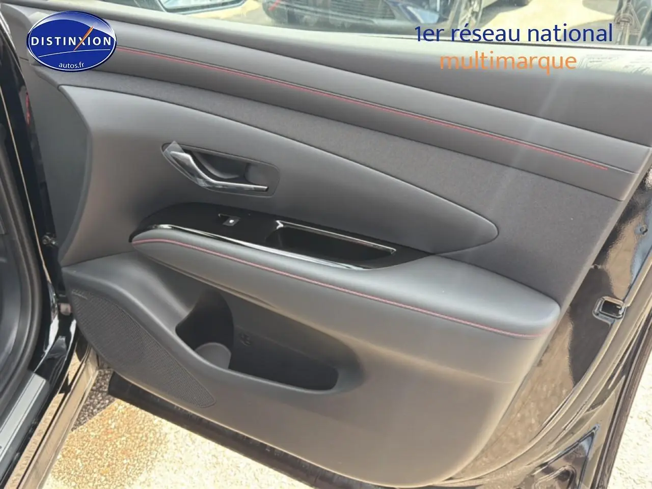 Gros plan sur la porte avant gauche noire du Hyundai Tucson 2026 avec surpiqûres rouges et poignée chromée.