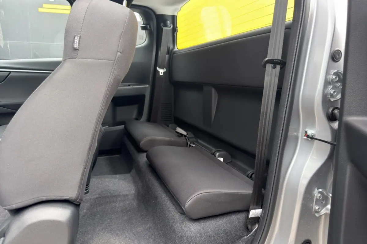 Vue intérieure côté droit du pick-up Isuzu D-MAX 2026, sièges arrière strapontins en tissu noir, carrosserie argentée visible.
