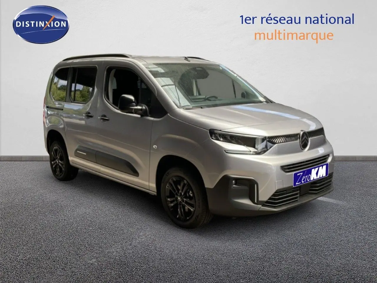 Vue 3/4 avant d'un Citroën Berlingo gris Artense métal avec jantes noires, présenté en intérieur showroom.