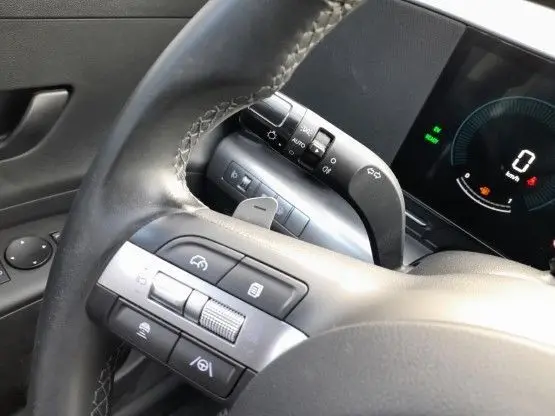 Gros plan sur le volant cuir noir et les commandes multifonctions du Hyundai Kona hybride 2024, tableau de bord digital visible.