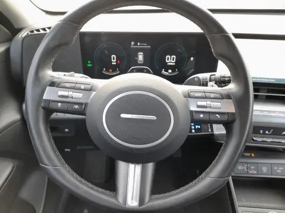 Vue centrée sur le volant cuir noir du Hyundai Kona 2024, avec tableau de bord numérique et commandes intégrées visibles.