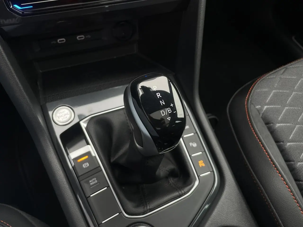 Le levier de vitesses automatique noir du SEAT Tarraco 2024, entouré de commandes et siège tissu gris à surpiqûres orange.