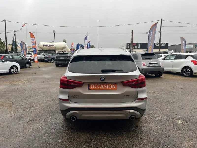 Vue arrière d'un BMW X3 xDrive30eA 292ch Lounge en Glacier Silver avec double sortie d'échappement sur parking.