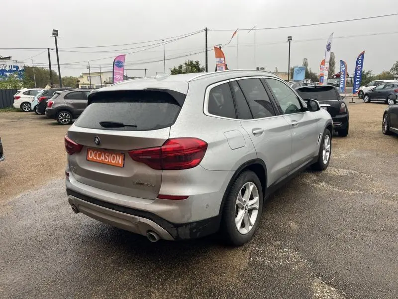 Vue 3/4 arrière droite d'un BMW X3 xDrive30e Glacier Silver avec double sortie d'échappement et vitres teintées.