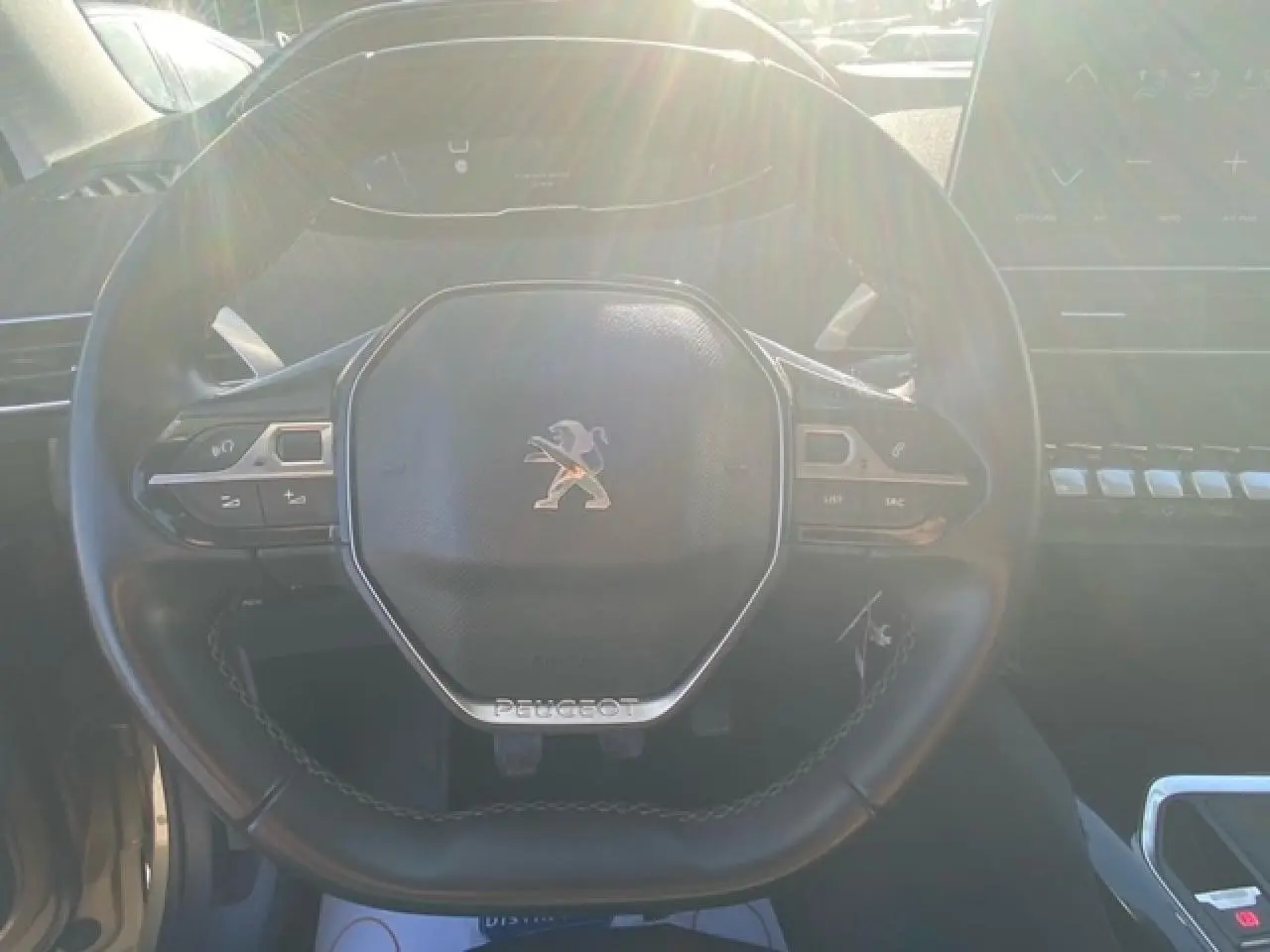 Vue rapprochée du volant compact noir de la Peugeot 3008 beige clair, avec commandes multifonctions visibles.