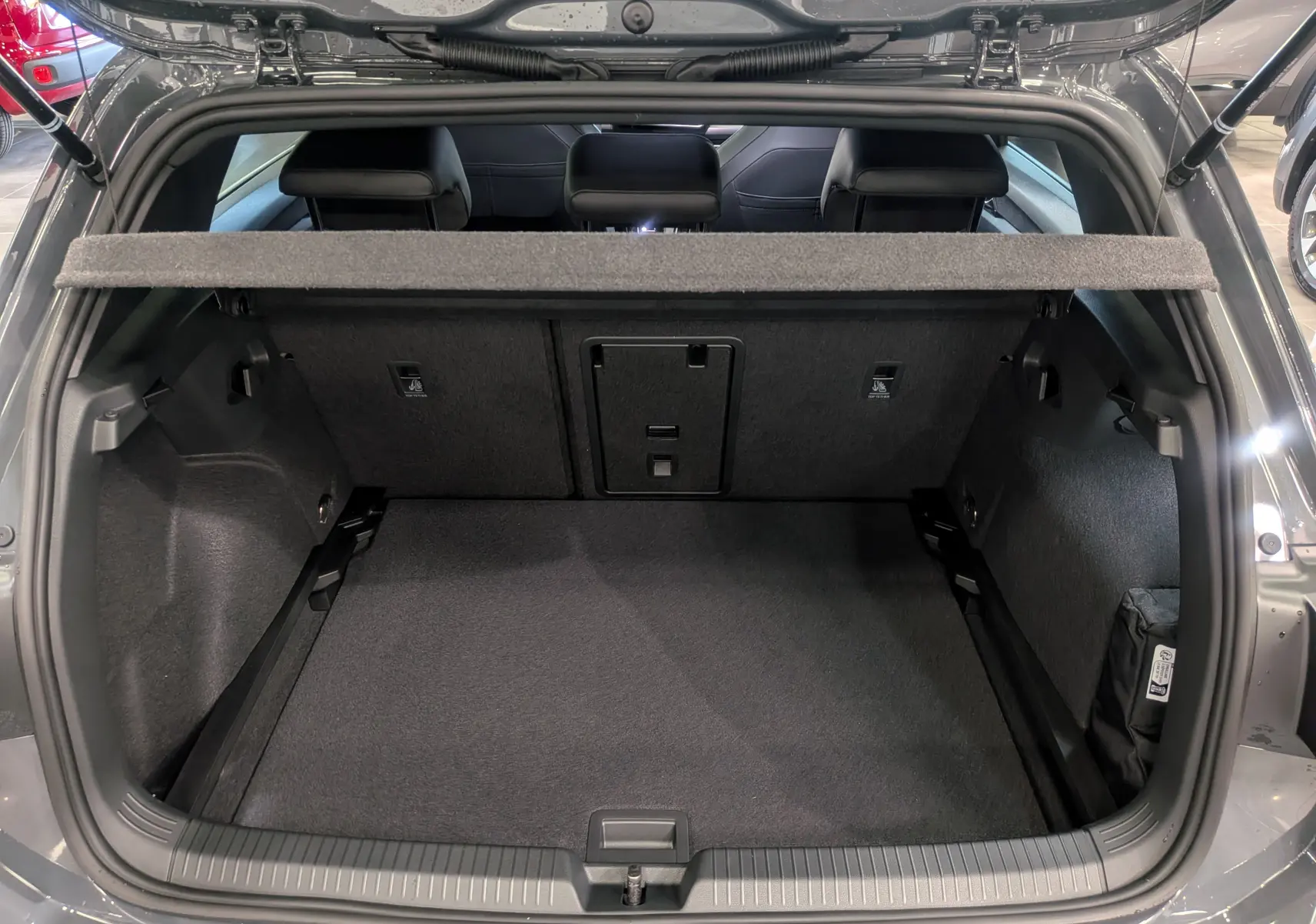 Vue arrière du coffre ouvert d'une Volkswagen Golf VIII gris Urano, montrant l'espace de chargement et la banquette arrière.