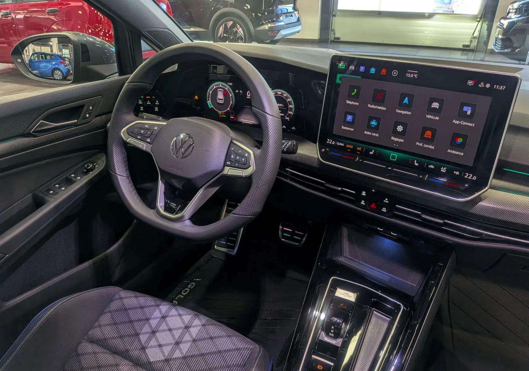 Vue intérieure côté conducteur de la Volkswagen Golf VIII gris Urano, avec tableau de bord digital et grand écran tactile central.