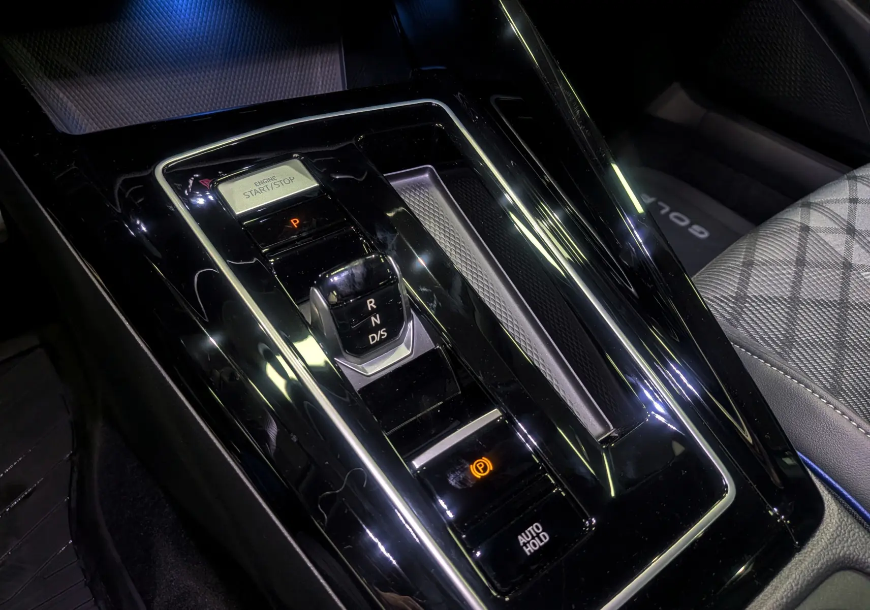 Vue rapprochée de la console centrale noire brillante avec levier de vitesses et bouton start/stop de la Volkswagen Golf VIII.