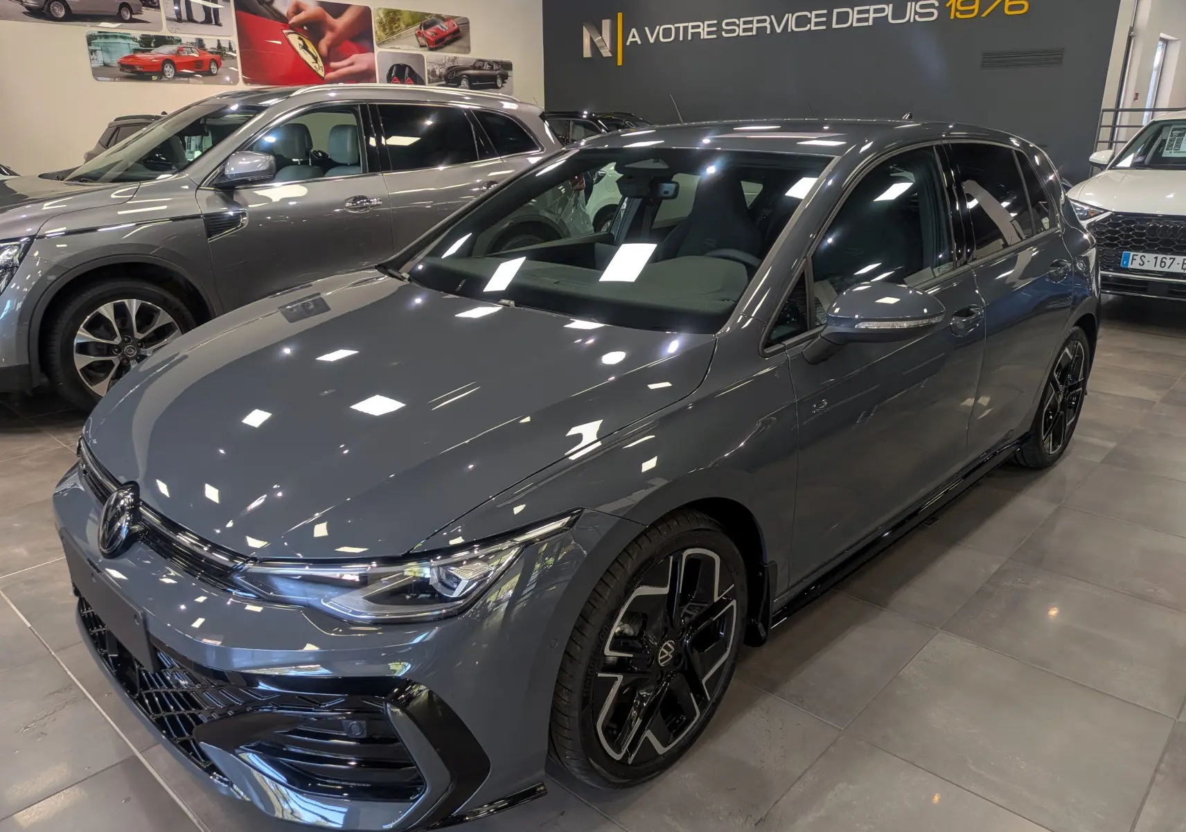 Volkswagen Golf VIII gris Urano vue 3/4 avant droit, avec jantes noires et détails R-Line visibles en showroom.