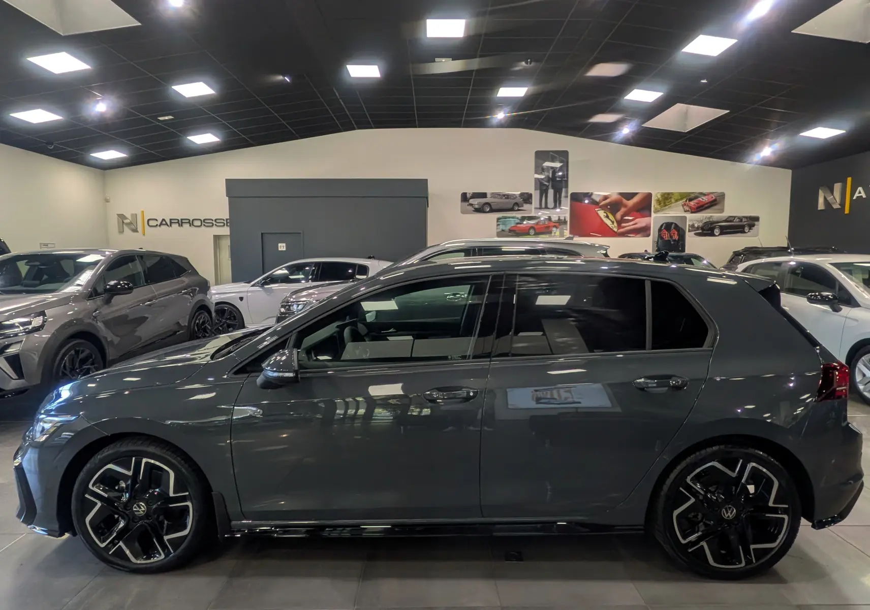 Vue de profil côté gauche d’une Volkswagen Golf VIII gris Urano, avec jantes noires et toit noir en showroom.