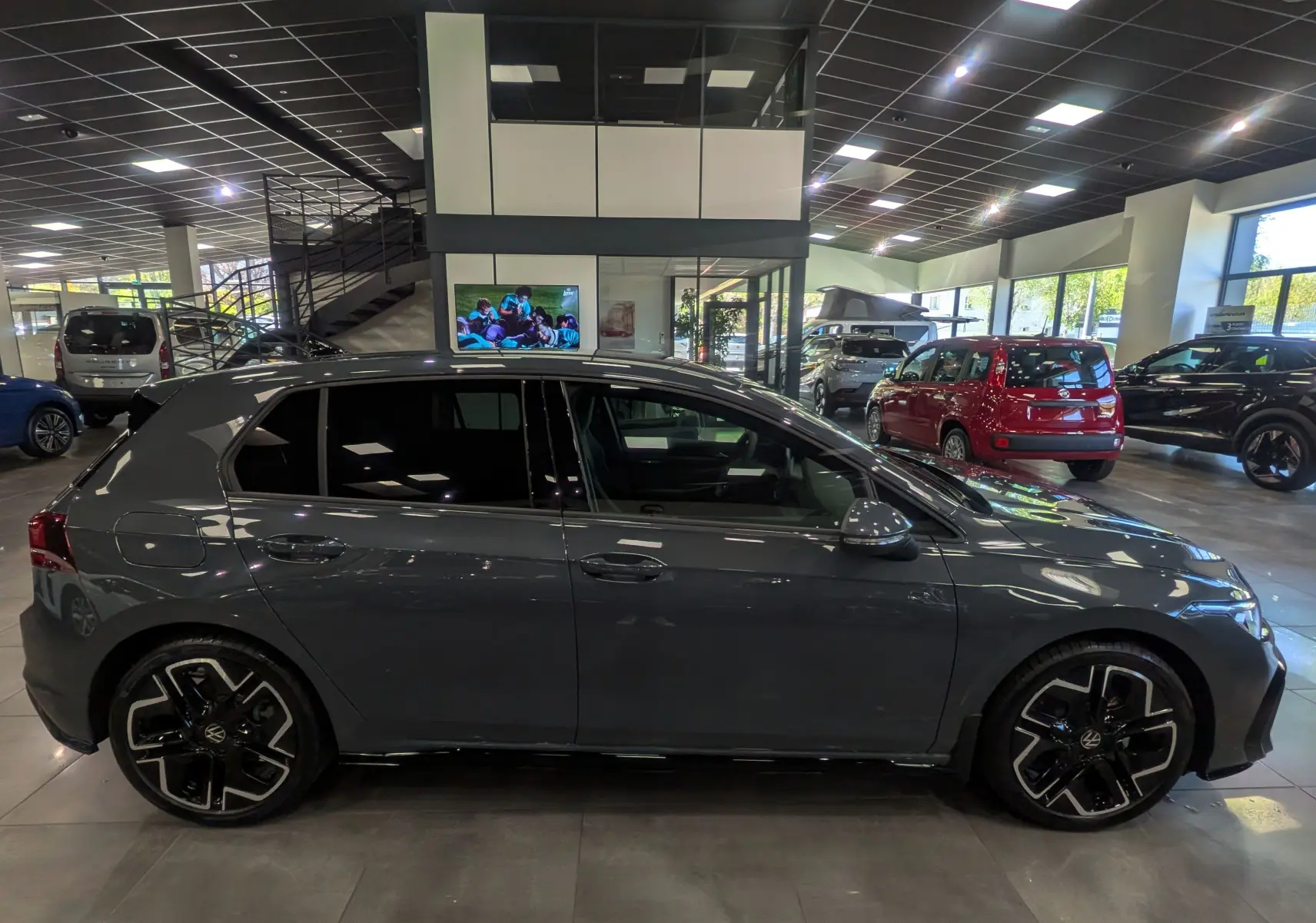 Volkswagen Golf VIII 1.5 eTSI R-Line gris Urano vue de profil côté gauche en intérieur showroom.