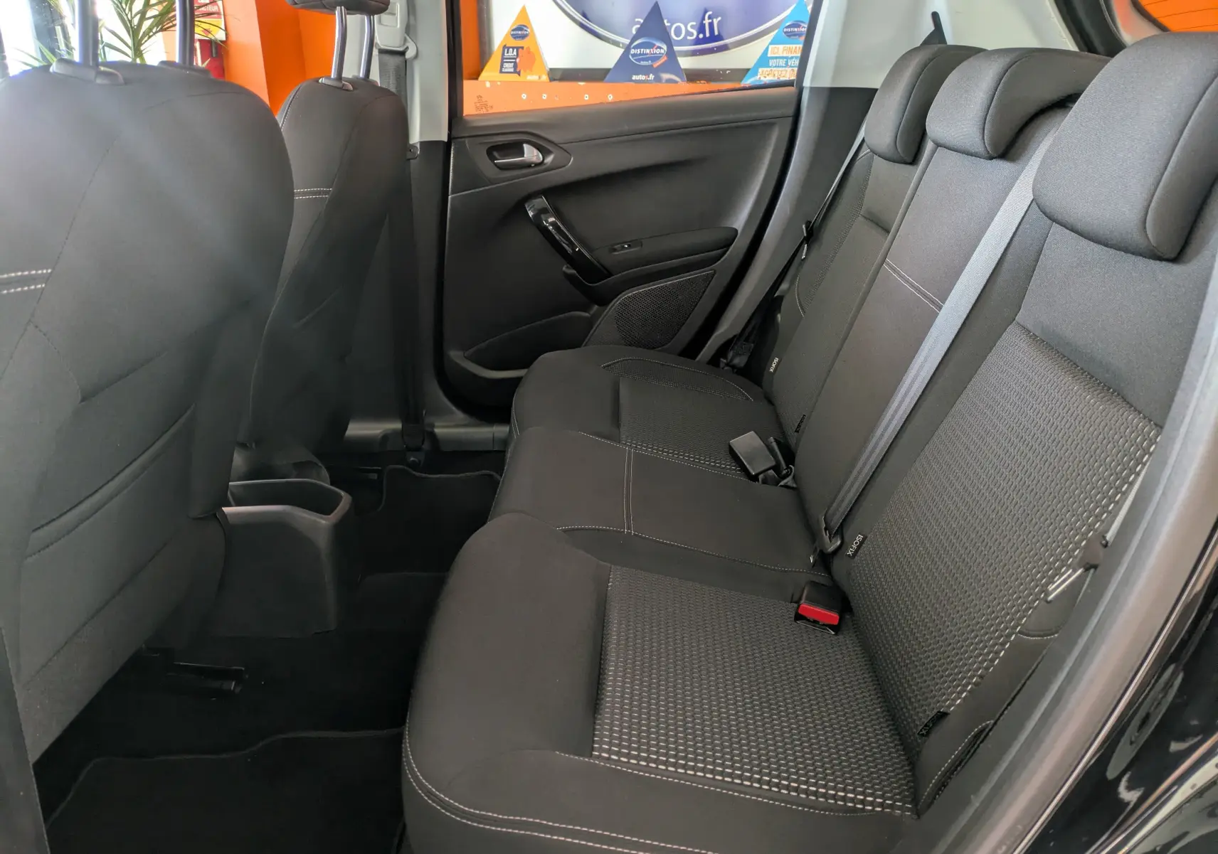 Vue intérieure côté droit des sièges arrière noirs en tissu de la Peugeot 208 Allure 2019, avec ceinture de sécurité et porte ouverte.