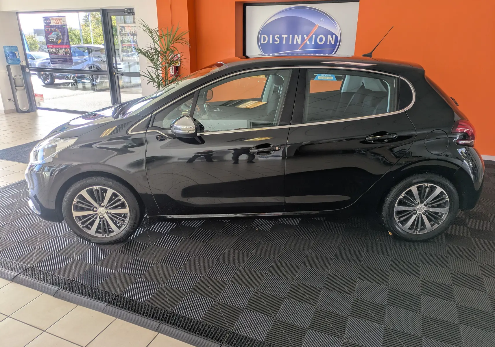 Profil côté gauche d'une Peugeot 208 Allure noire de 2019, cinq portes, avec jantes alliage bicolores, en intérieur showroom.