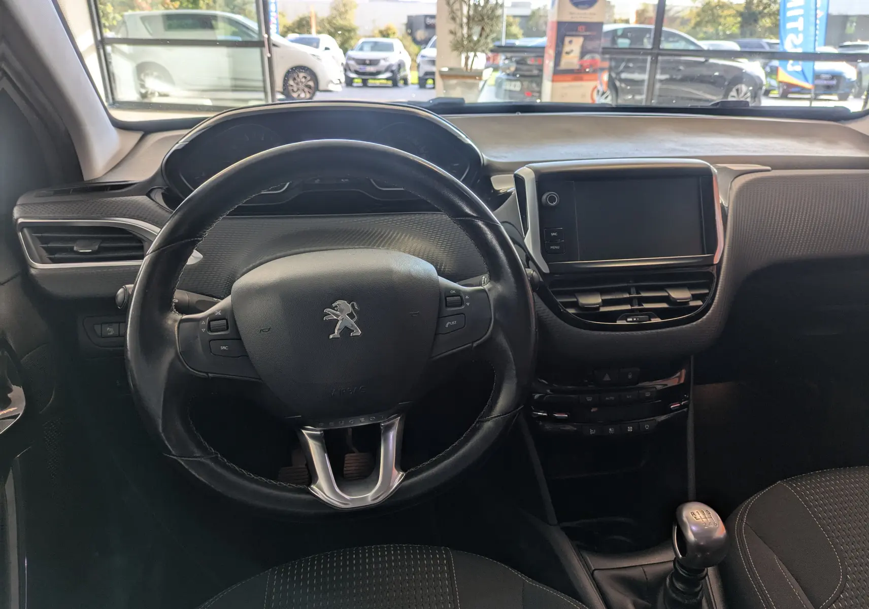 Intérieur de la Peugeot 208 Allure 2019, vue centrée sur le volant cuir noir et la console avec écran tactile.
