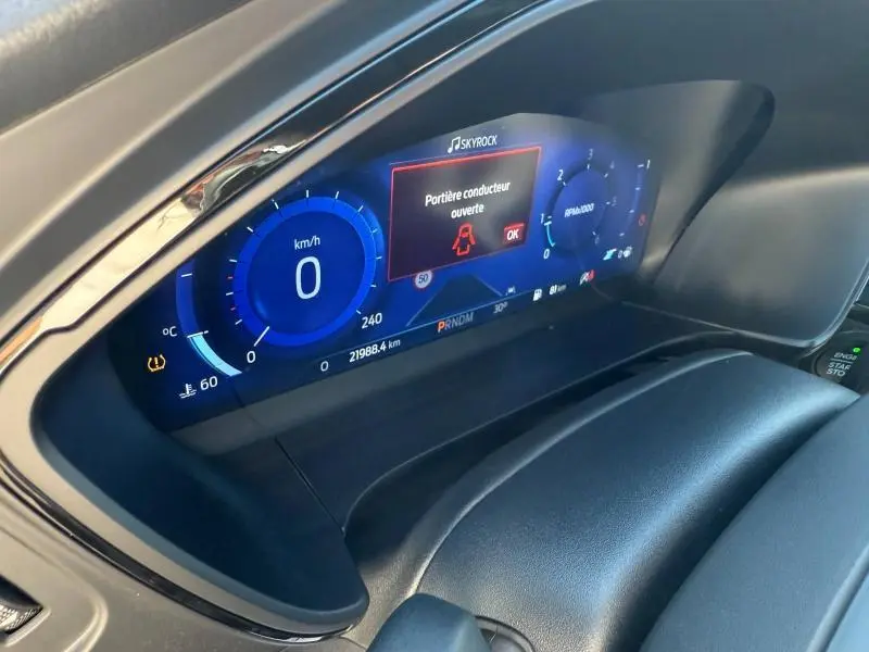 Vue rapprochée du tableau de bord numérique bleu du Ford Kuga 2024, affichant une alerte porte ouverte côté conducteur.