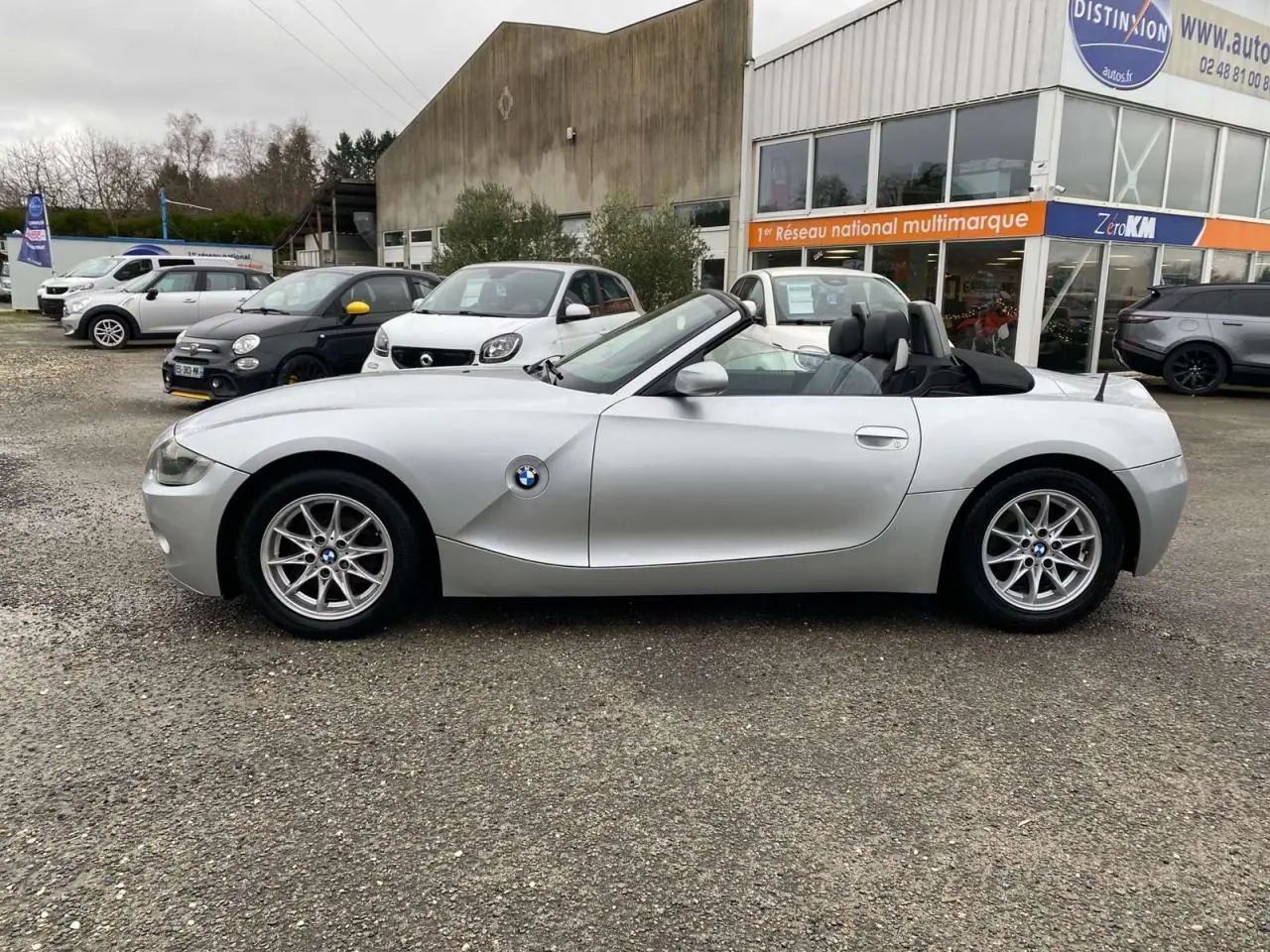 BMW Z4 Roadster gris clair vue de profil côté gauche, capote noire ouverte et jantes alliage 16 pouces visibles.
