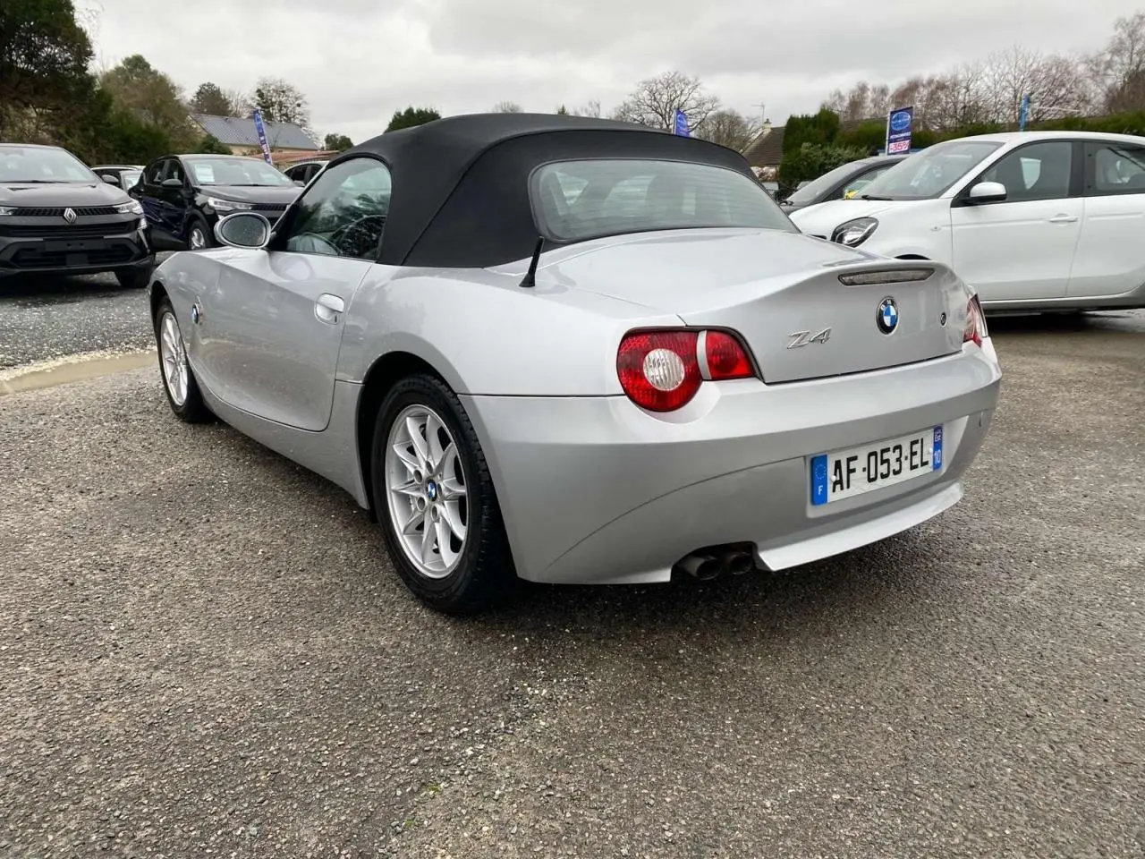 BMW Z4 Roadster gris clair vue 3/4 arrière avec capote noire et double sortie d’échappement visible.