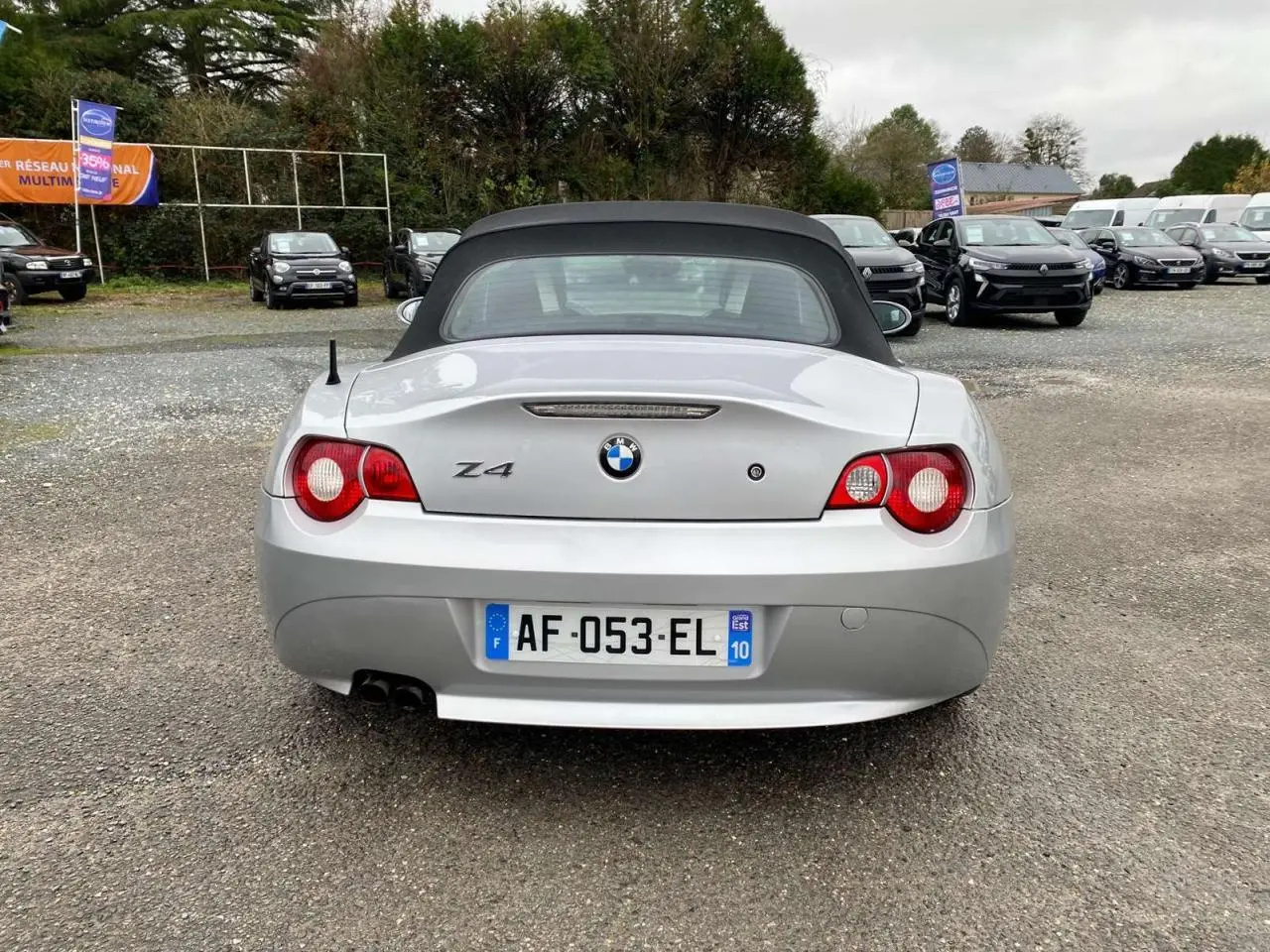 Vue arrière d'une BMW Z4 gris clair avec capote noire relevée et double sortie d'échappement visible.