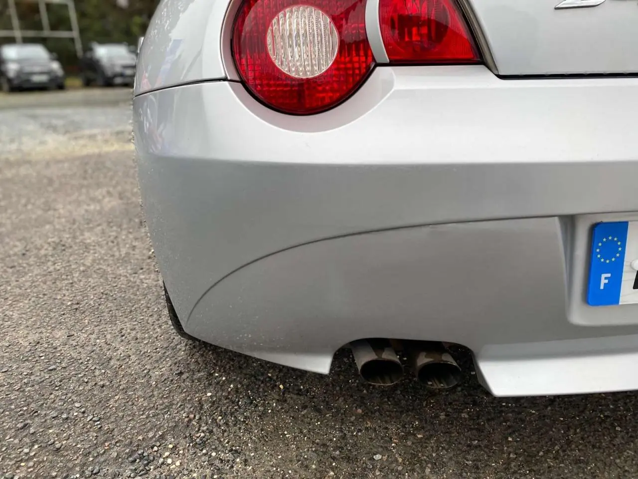 Gros plan sur l'arrière droit d'une BMW Z4 Roadster gris clair, avec double sortie d'échappement et feu arrière rond rouge.