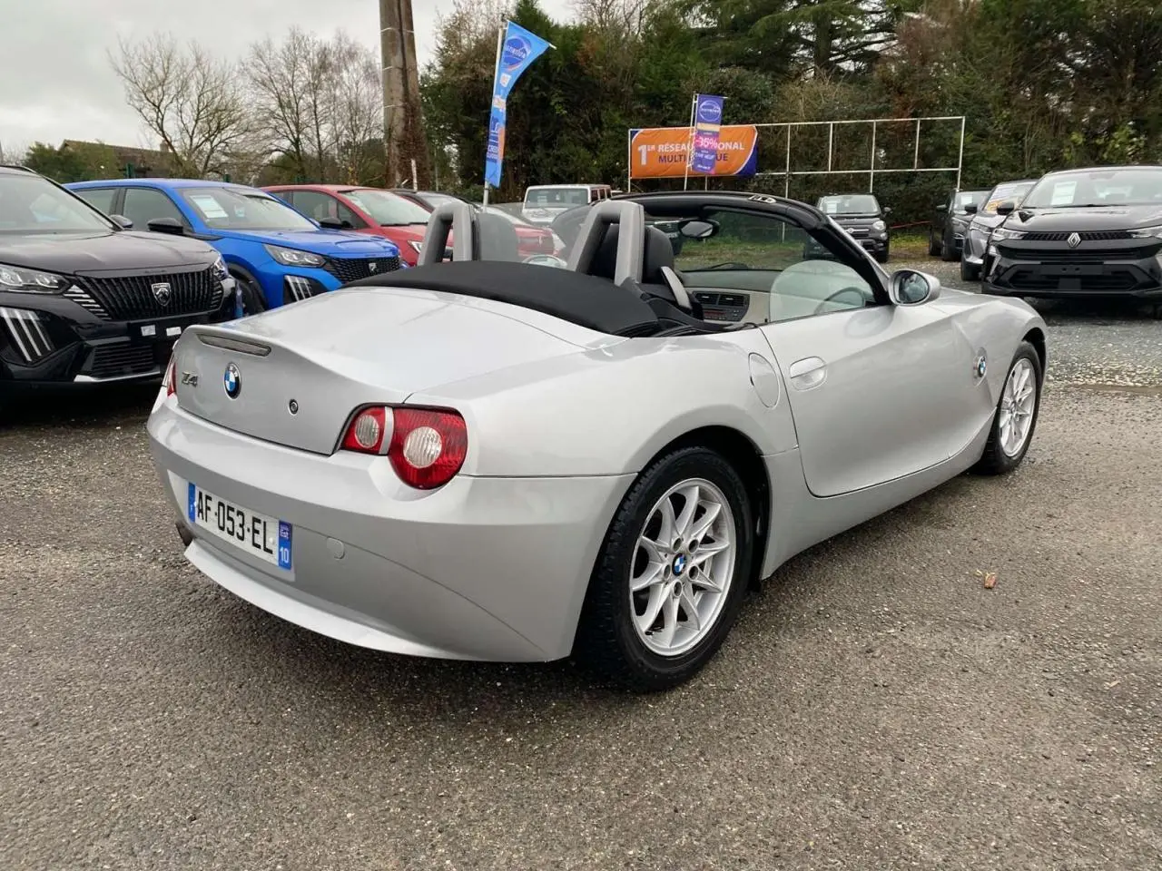 BMW Z4 Roadster gris clair vue 3/4 arrière droit, capote noire fermée et jantes alliage 16 pouces visibles.