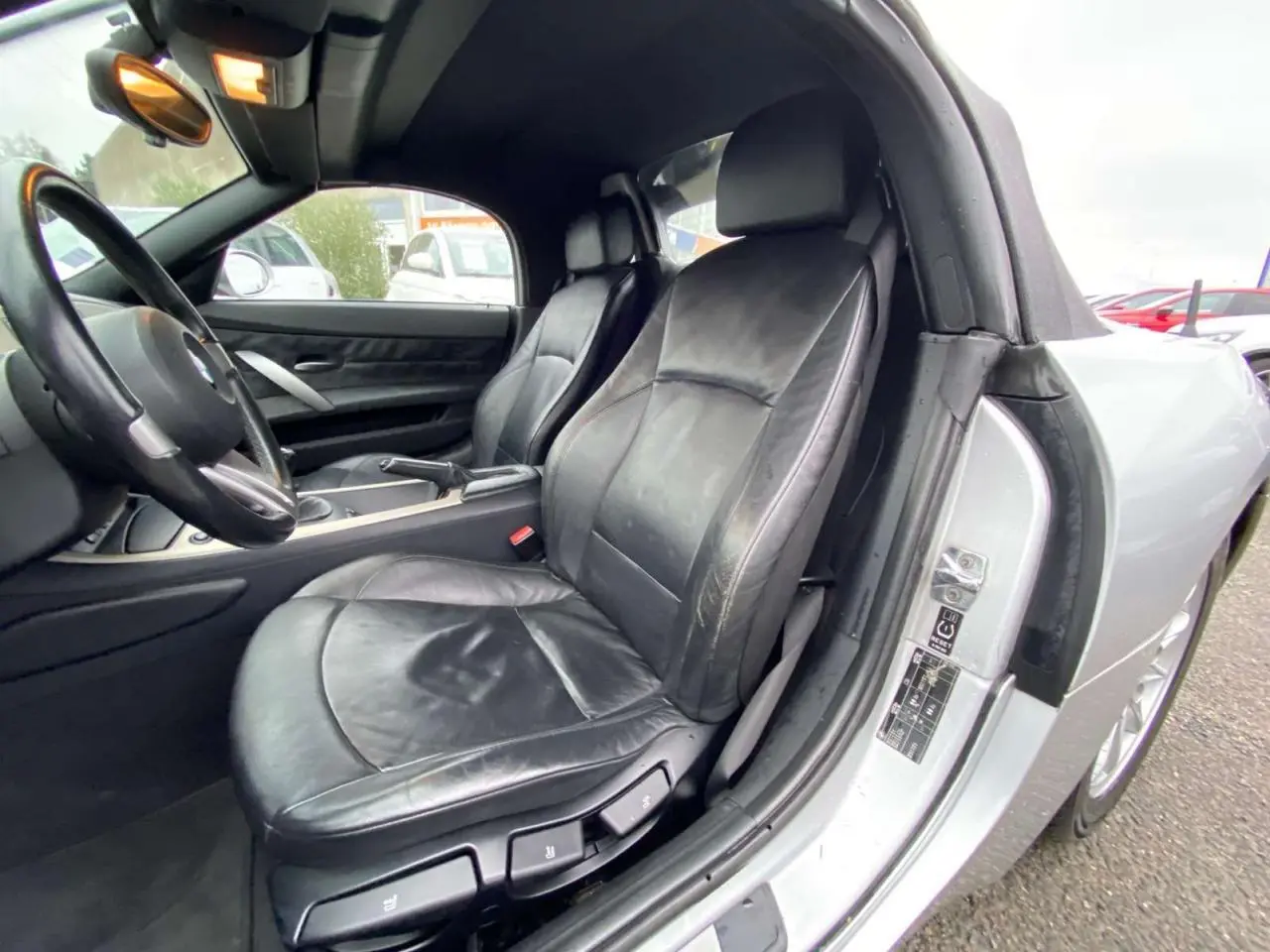 Vue intérieure côté conducteur d'une BMW Z4 Roadster gris clair de 2005 avec sièges cuir noirs et volant sport.