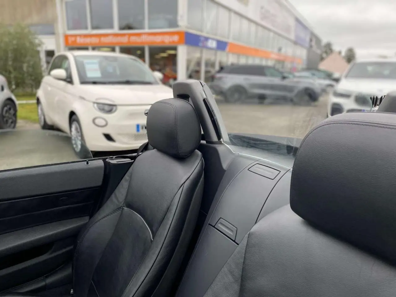 Vue intérieure rapprochée des sièges avant en cuir noir d’un BMW Z4 Roadster gris clair avec coupe-vent transparent.