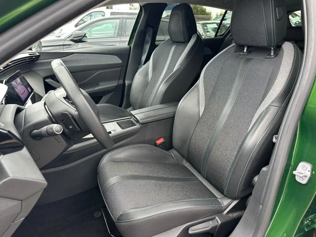 Vue intérieure côté conducteur de la Peugeot 308 2023 vert foncé, sièges tissu et cuir avec accoudoir central.
