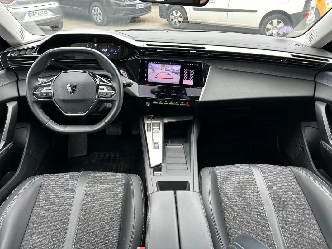 Vue intérieure avant de la Peugeot 308 2023, tableau de bord moderne avec écran tactile et volant compact noir.