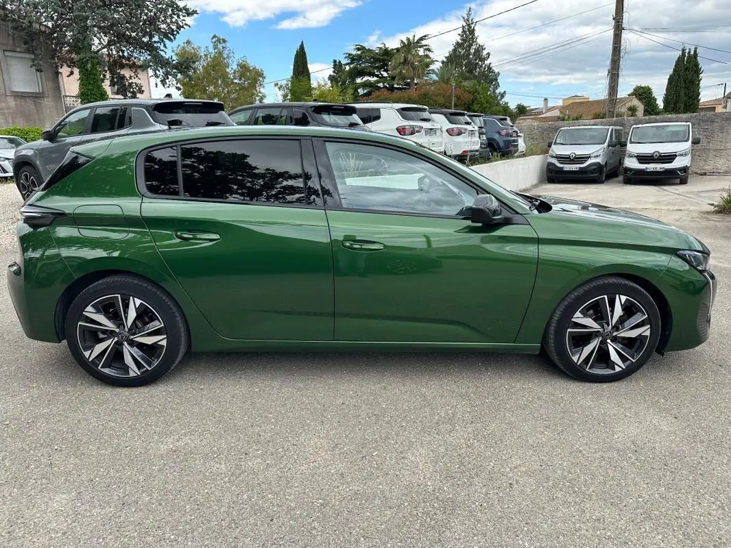 Vue de profil côté gauche d'une Peugeot 308 2023 vert foncé avec jantes alliage 17 pouces sur parking.