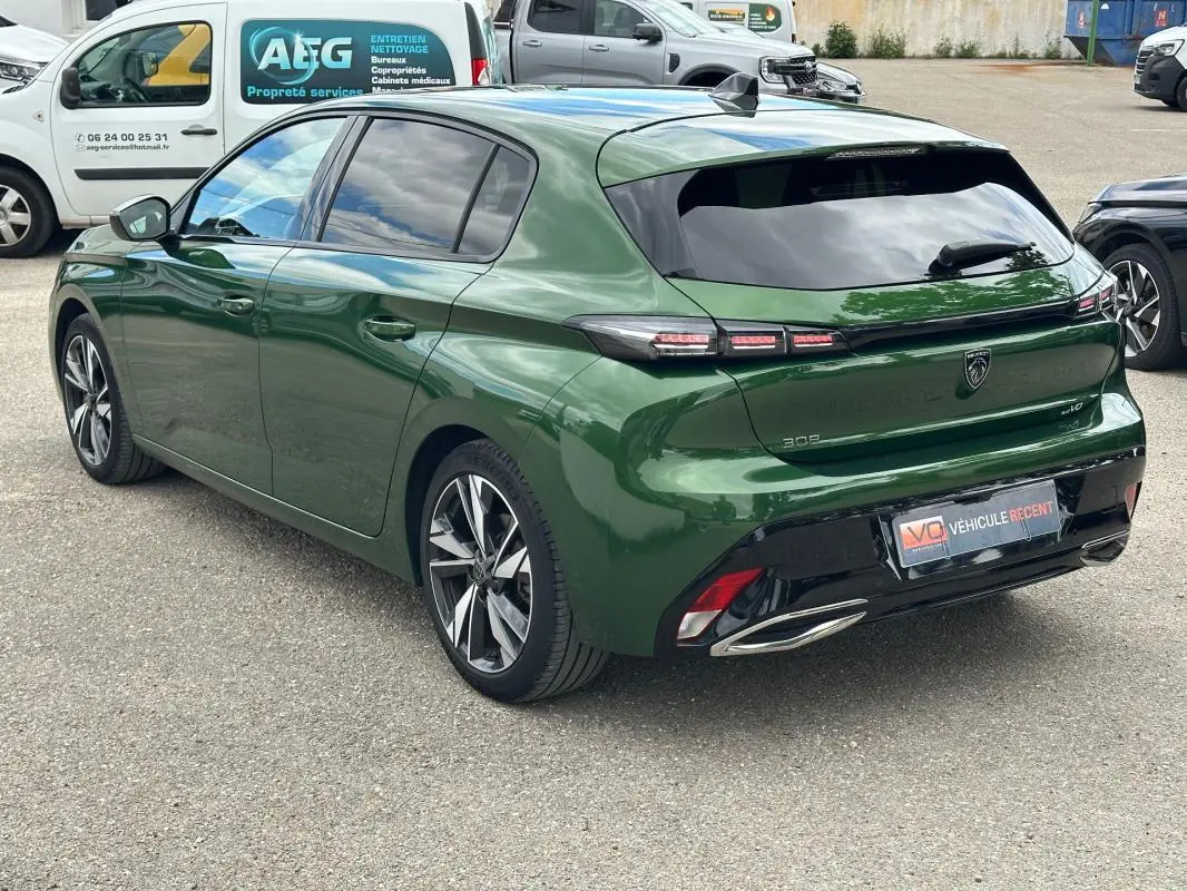 Vue 3/4 arrière droite d'une Peugeot 308 2023 vert foncé avec jantes alliage 17 pouces et feux arrière LED distinctifs.