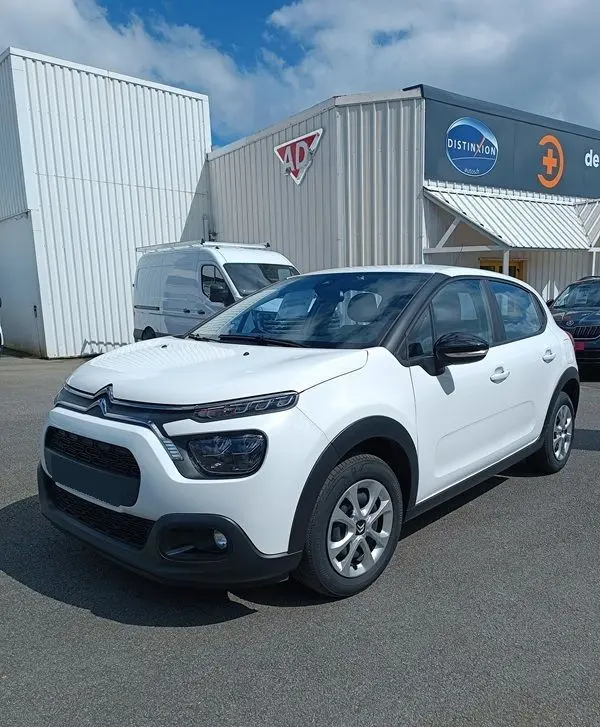 Citroën C3 Société blanche vue 3/4 avant droit, avec rétroviseurs noirs et jantes acier, stationnée devant un bâtiment industriel.