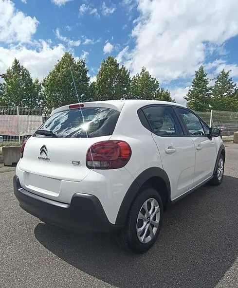 Vue 3/4 arrière droite d'une Citroën C3 Société blanche 2023 avec feux arrière rouges et protections noires sur pare-chocs.