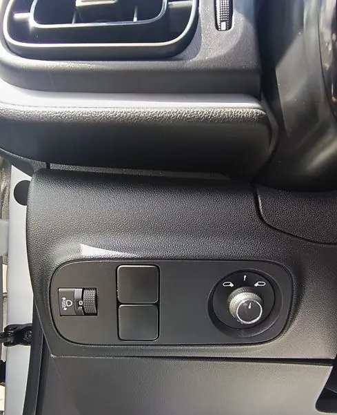 Vue rapprochée du panneau de réglage des phares et des rétroviseurs côté conducteur d'une Citroën C3 Société blanche 2023.