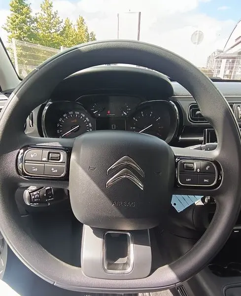 Vue rapprochée du volant noir de la Citroën C3 Société 2023 avec commandes intégrées et tableau de bord visible.
