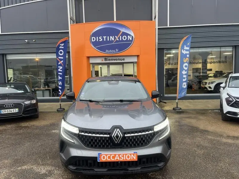 Vue frontale d'un Renault Austral gris métallisé avec calandre noire et phares LED allumés devant un concessionnaire Distinxion.