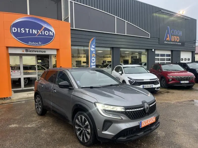 Renault Austral gris 3/4 avant droit garé devant un concessionnaire avec panneau orange Distinxion visible