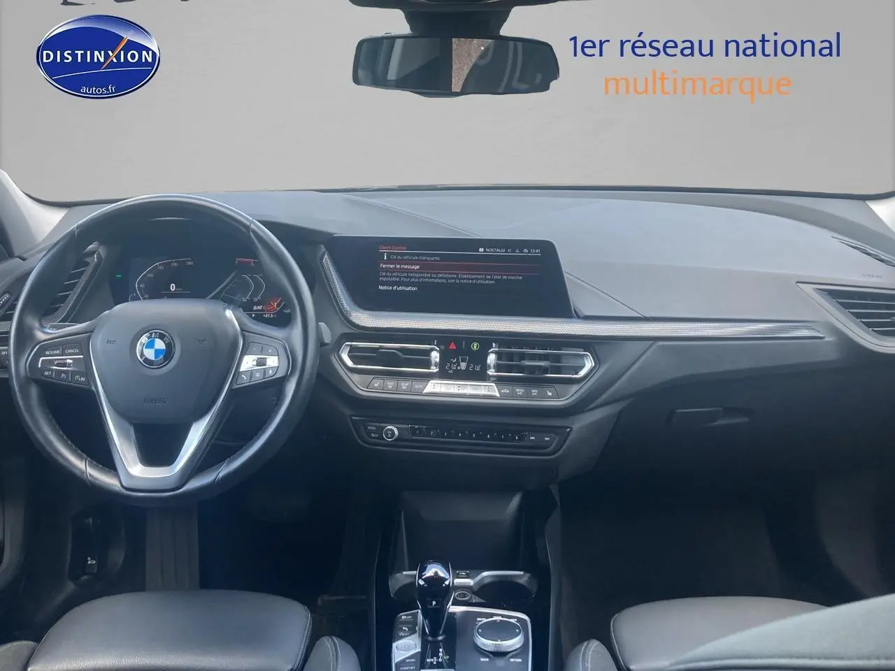 Vue frontale de l'intérieur de la BMW Série 1 noire 2023, volant sport cuir et écran central du tableau de bord.