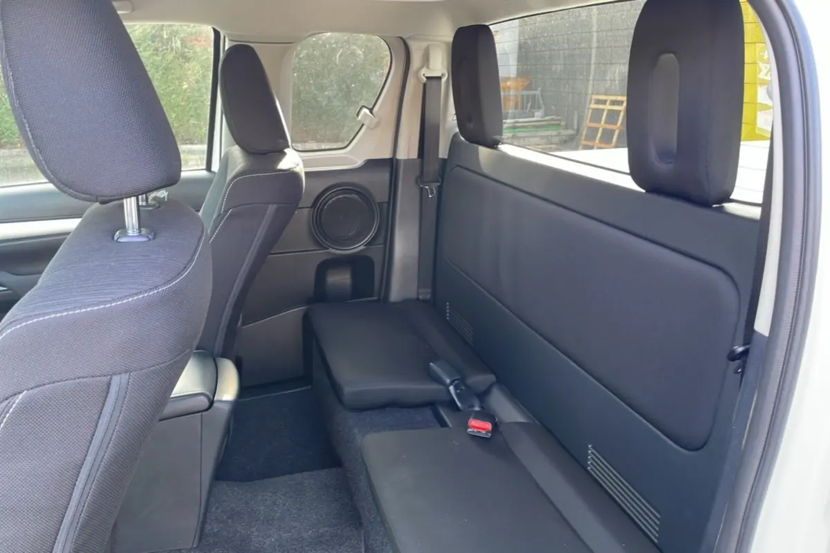 Intérieur arrière du Toyota Hilux 4x4 blanc pur 2025, vue côté droit sur les sièges noirs et la porte arrière ouverte.