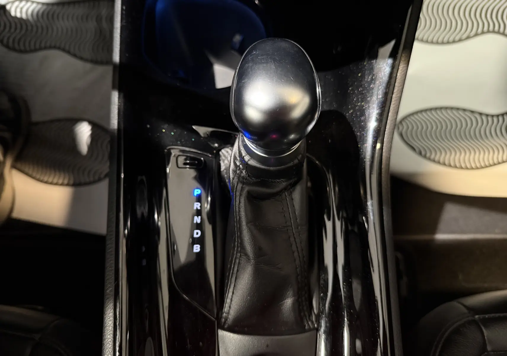 Gros plan sur le levier de vitesses automatique noir brillant du Toyota C-HR Hybride, avec indication des modes éclairés en bleu.