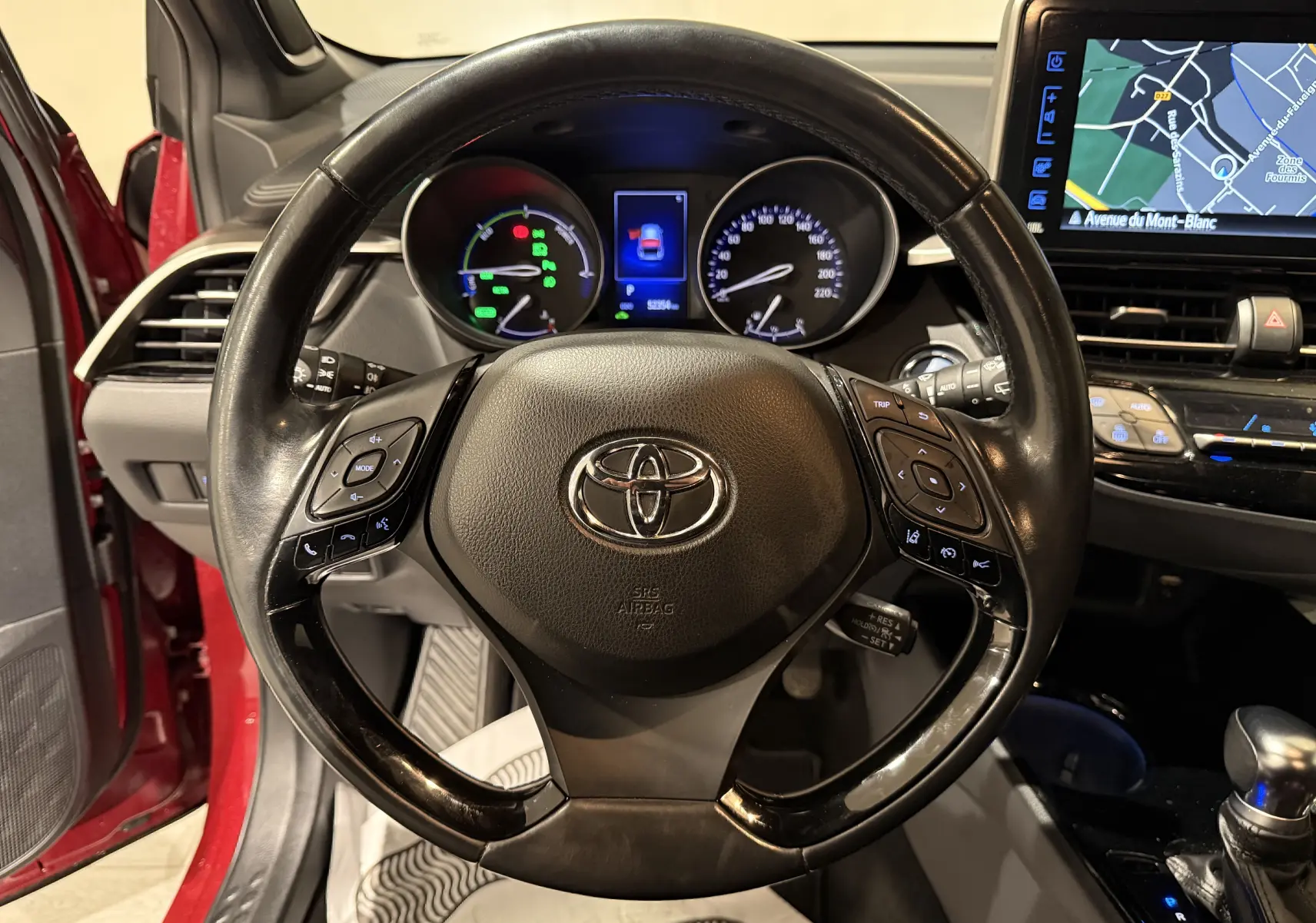 Vue intérieure centrée sur le volant noir du Toyota C-HR hybride rouge de 2018 avec tableau de bord et écran GPS visibles.