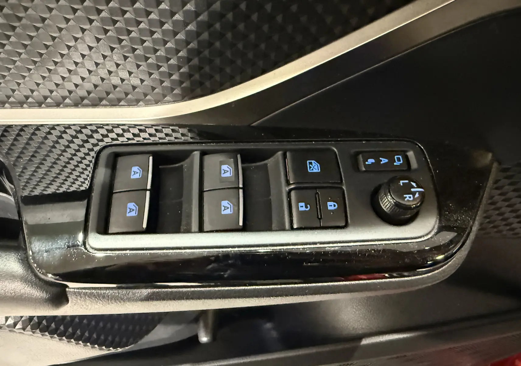 Gros plan sur les commandes électriques des vitres et rétroviseurs côté conducteur du Toyota C-HR Hybride rouge de 2018.