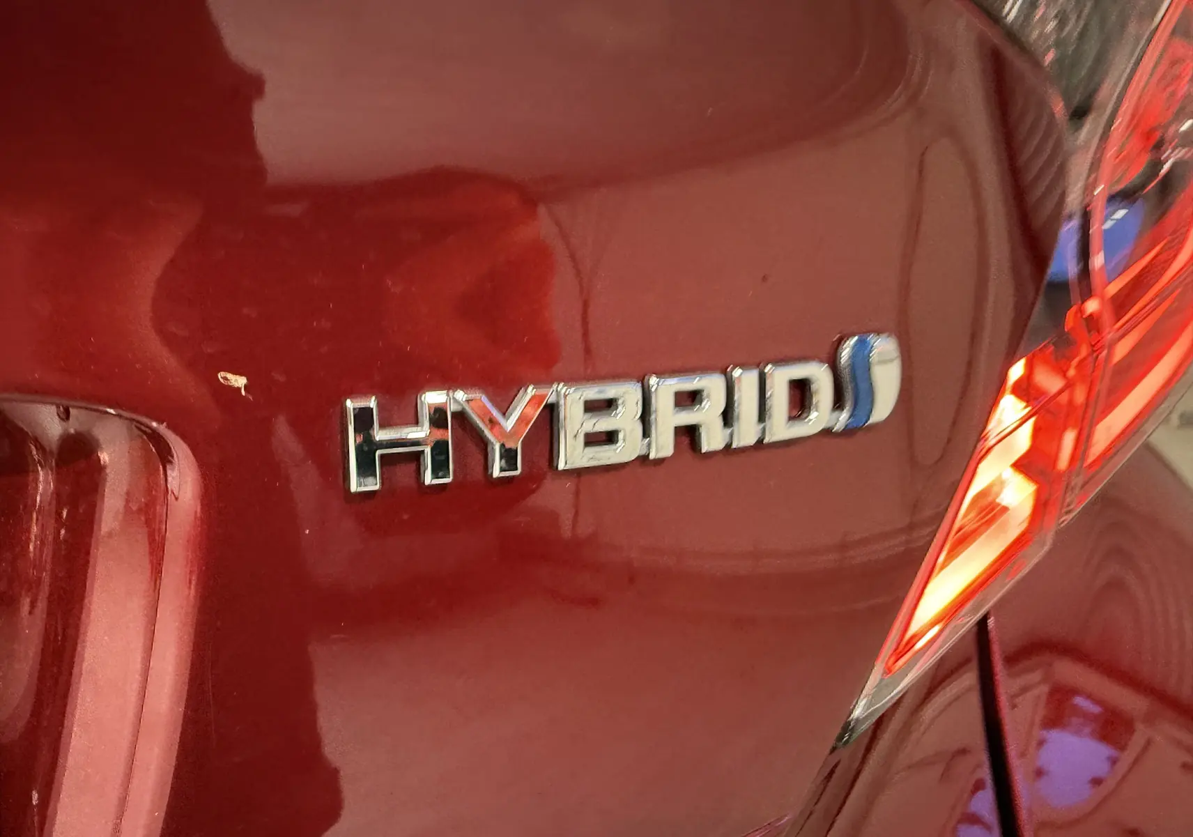 Gros plan sur l'arrière droit rouge d'un Toyota C-HR hybride avec le badge "HYBRID" et un feu arrière allumé.