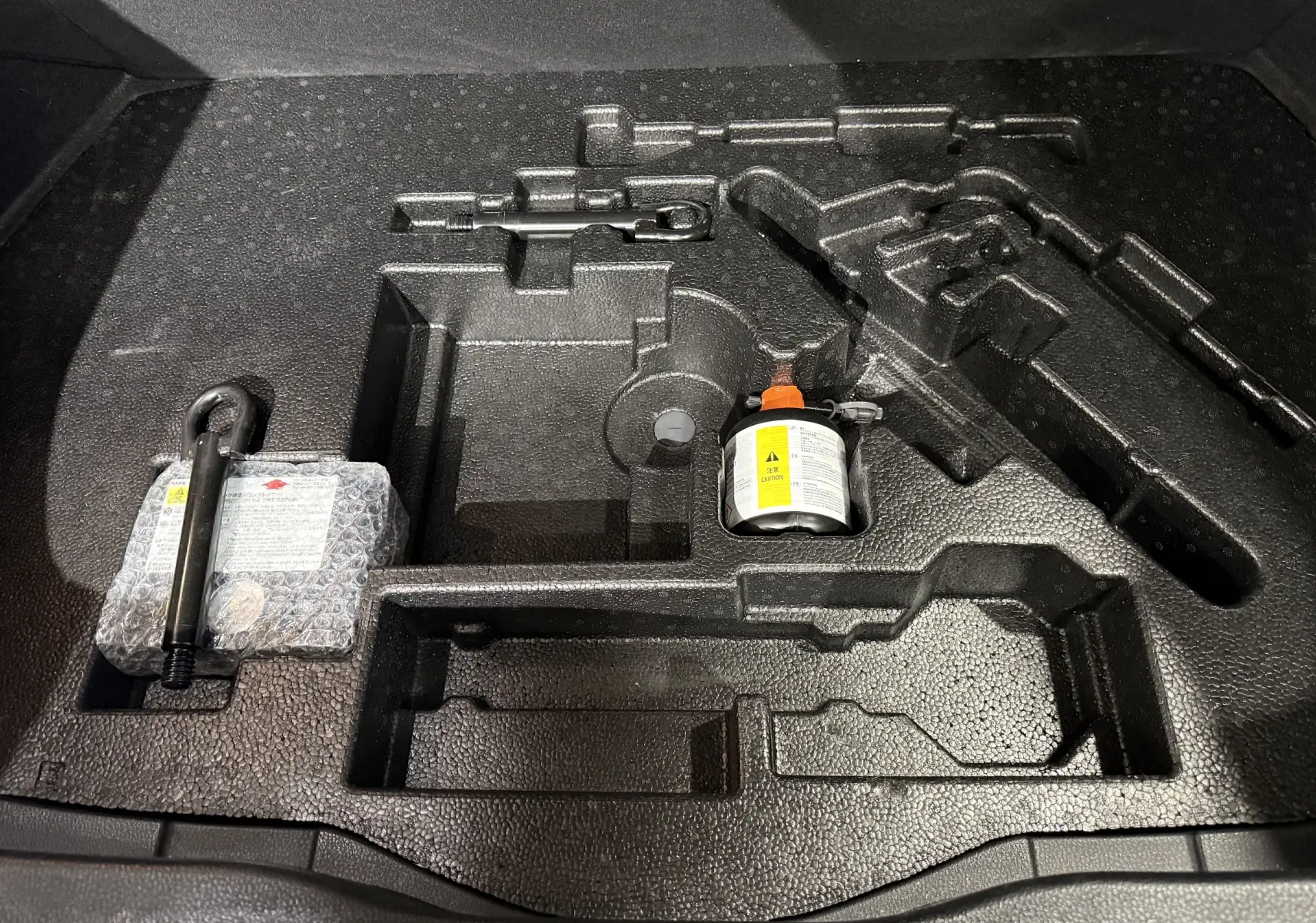 Rangement en mousse noire dans le coffre du Toyota C-HR Hybride 2018, contenant un kit de réparation pneu et outils.